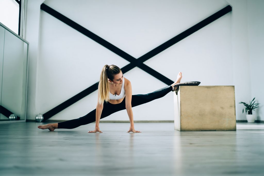Confident adult barefoot woman doing side split exercise in sport club